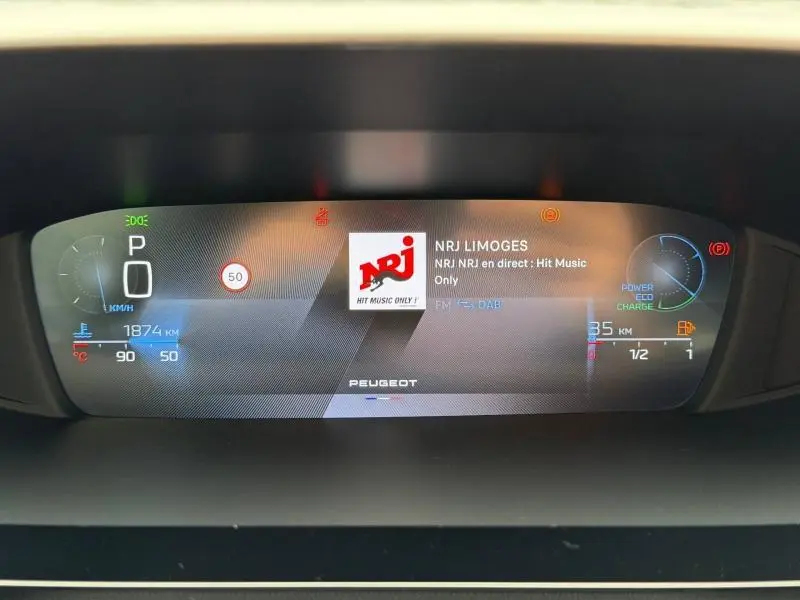 Affichage numérique du tableau de bord Peugeot 308 Hybrid blanc, avec radio NRJ et indicateurs de vitesse et énergie.