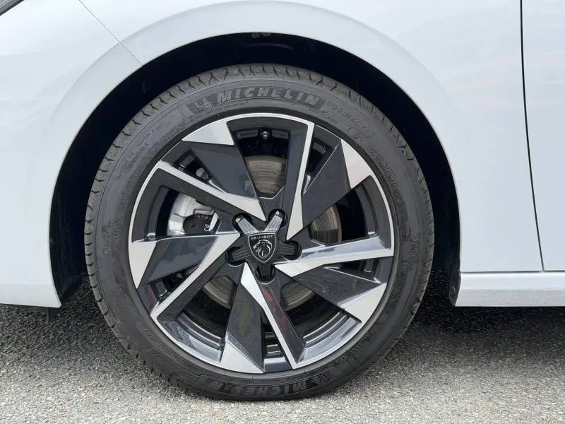 Gros plan sur la jante alliage bicolore noire et argentée de la Peugeot 308 blanche Okénite 2025.