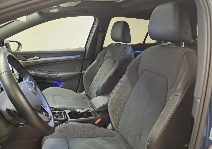 Vue intérieure côté conducteur de la Volkswagen Golf 1.5 eTSI 2024 avec sièges noirs et éclairage d'ambiance bleu.