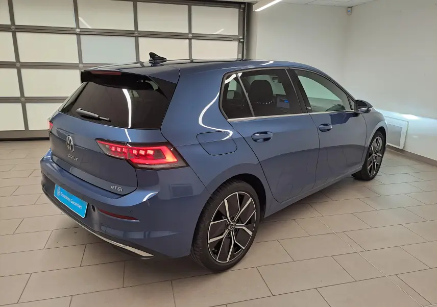 Volkswagen Golf 1.5 eTSI 150 DSG7 Bleu Anémone vue 3/4 arrière droit avec feux LED allumés en intérieur.
