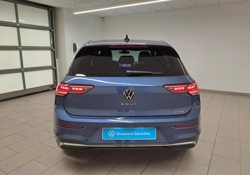 Vue arrière d'une Volkswagen Golf 1.5 eTSI 150 DSG7 Bleu Anémone avec feux LED allumés dans un garage.
