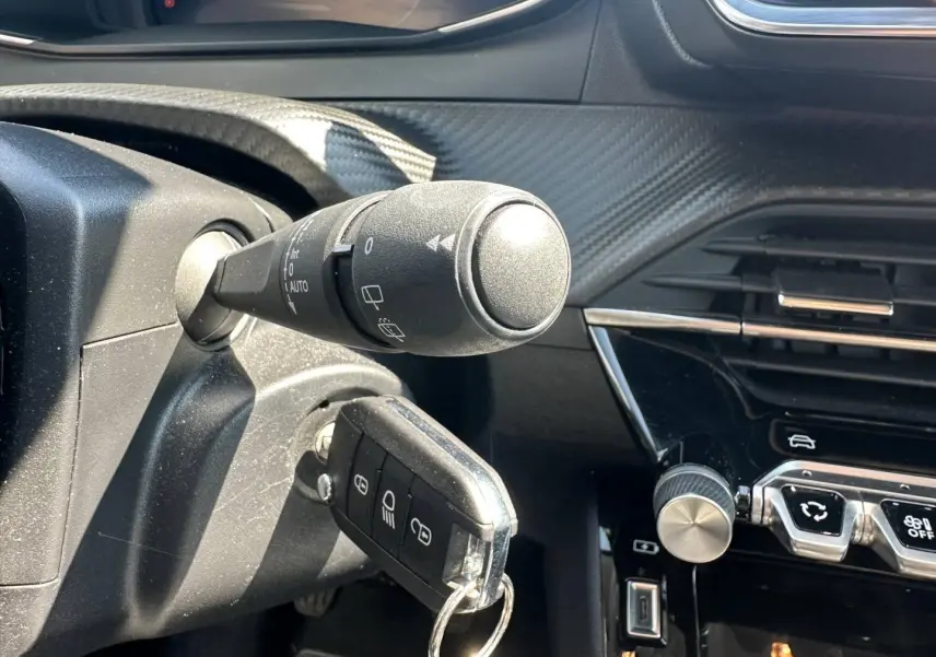 Gros plan sur le contacteur avec clé insérée dans une Peugeot 208 gris Selenium, tableau de bord noir et commandes centrales visibles.