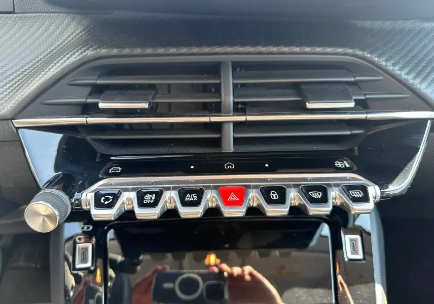 Gros plan sur la console centrale de la Peugeot 208 2025, boutons chromés et écran tactile noir brillant.