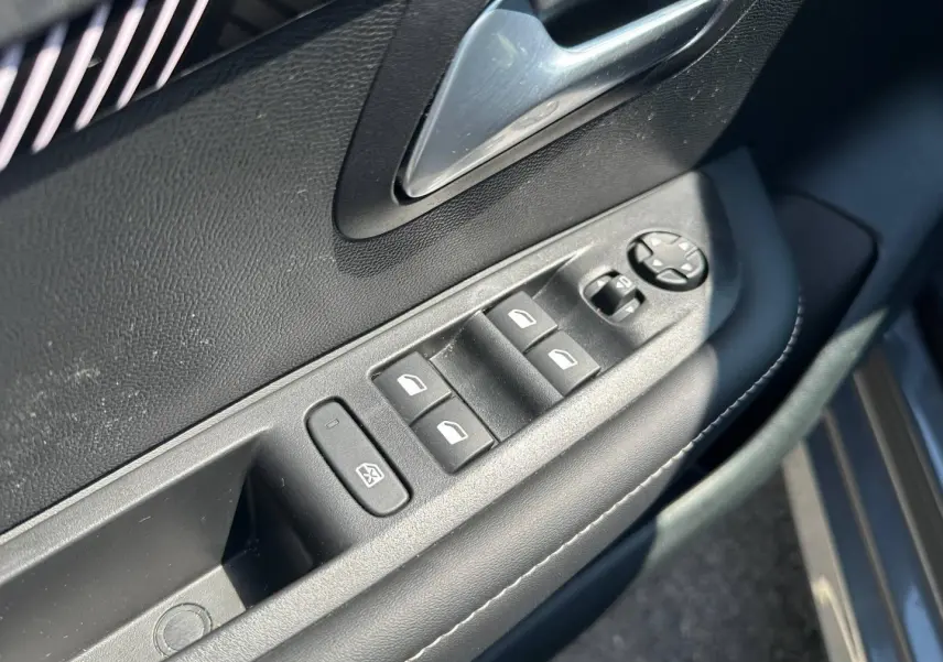 Détail des commandes de lève-vitres et rétroviseurs sur la porte côté gauche d’une Peugeot 208 gris Selenium.