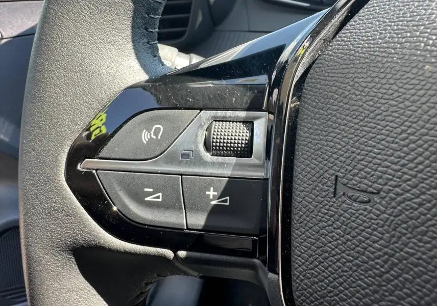 Gros plan sur les commandes noires du volant de la Peugeot 208 2025, avec boutons de volume et fonction mains-libres.