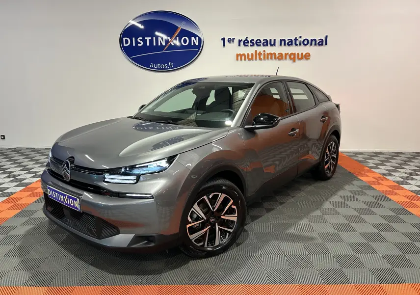 Citroën E-C4 électrique gris foncé en 3/4 avant droit, avec jantes noires et phares LED allumés en showroom.