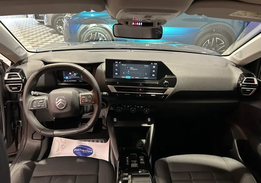 Vue intérieure avant du Citroën E-C4 gris foncé 2025, avec tableau de bord numérique et écran tactile central lumineux.
