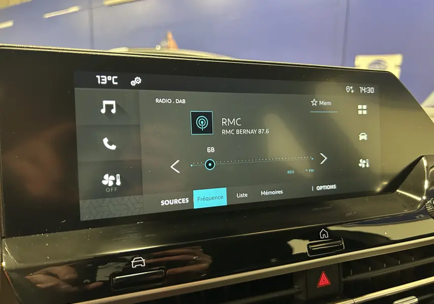 Écran tactile central du tableau de bord de la Citroën E-C4 gris foncé, affichant la radio RMC à 14h30.