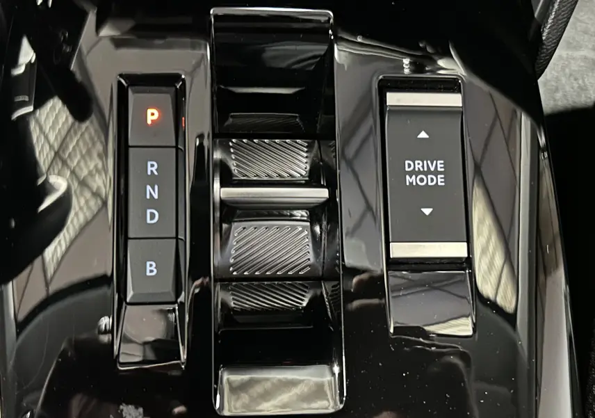 Gros plan sur la console centrale noire brillante de la Citroën E-C4 2025 avec commandes de boîte auto et mode de conduite.