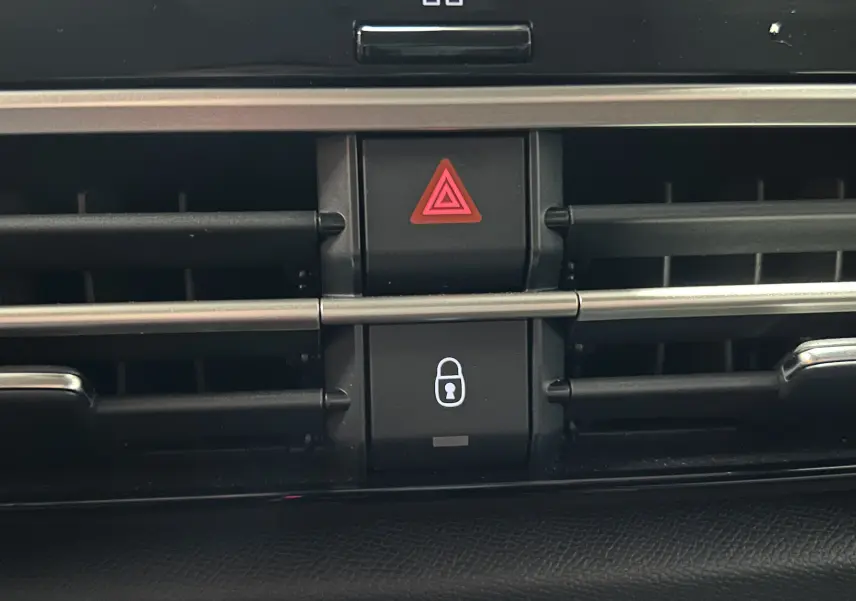 Gros plan sur les boutons de verrouillage centralisé et warning intégrés à la grille d'aération intérieure du Citroën E-C4 gris foncé.