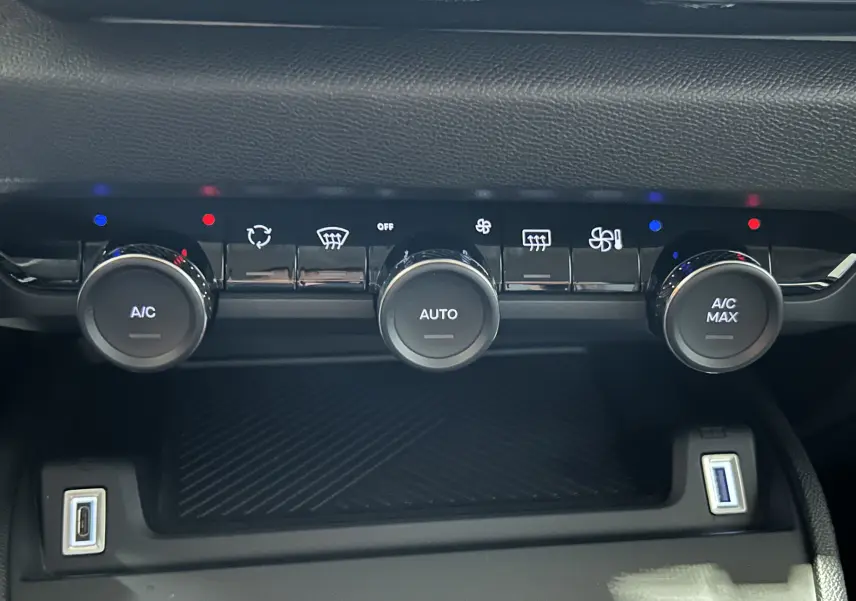 Gros plan sur la console centrale du Citroën E-C4 2025, montrant les commandes de climatisation automatique et deux ports USB.