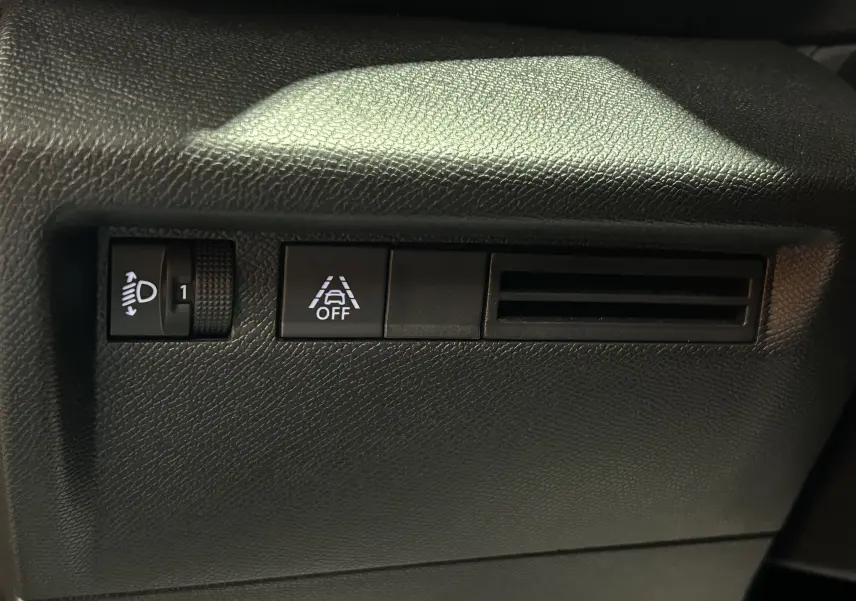 Détail intérieur du tableau de bord côté gauche du Citroën E-C4 2025, avec réglage des phares et bouton de désactivation de l'alerte de franchissement de ligne.
