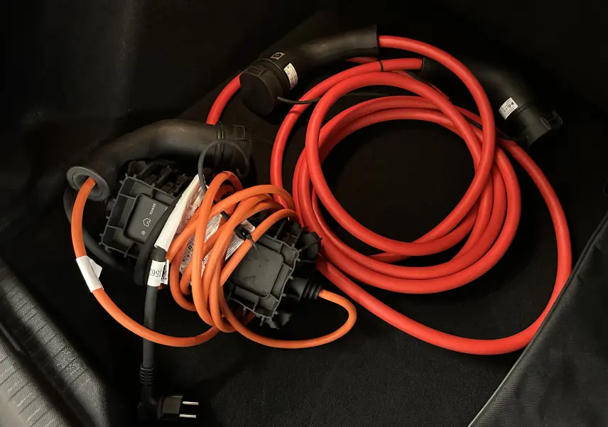 Câbles de recharge électrique rouge et orange enroulés dans le coffre d’une Citroën E-C4 gris foncé 2025.