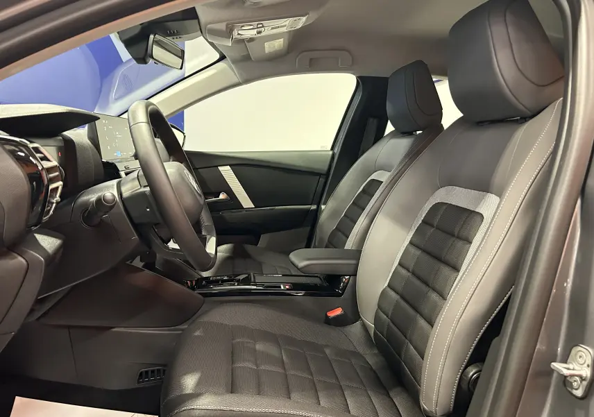 Vue intérieure côté conducteur de la Citroën E-C4 2025, sièges gris et noir avec console centrale moderne.