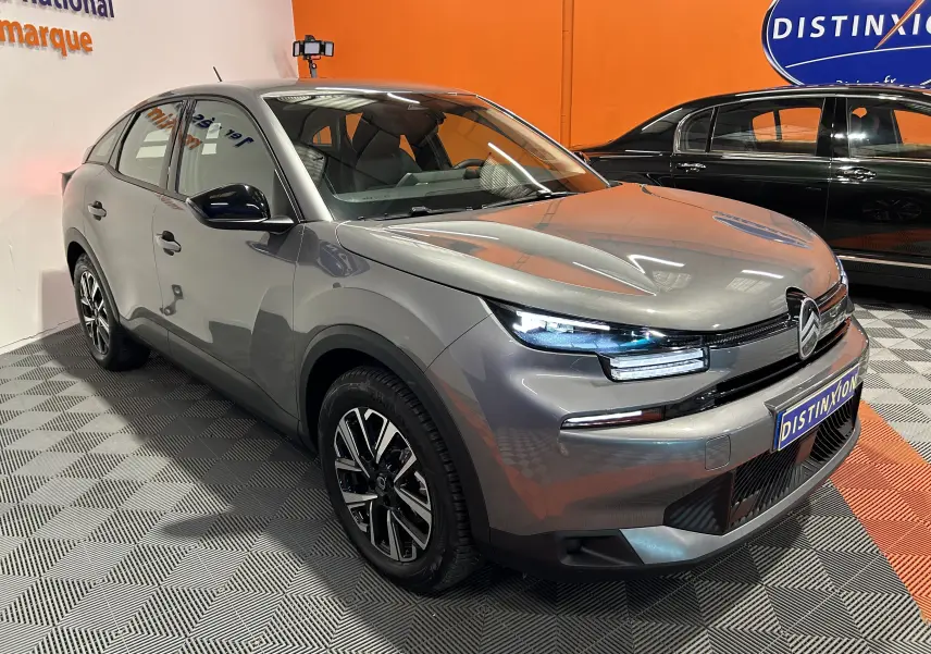 Citroën E-C4 gris foncé en 3/4 avant droit, phares LED allumés, jantes noires et détails modernes visibles.
