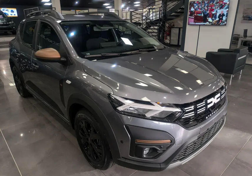 Vue 3/4 avant droite d'une Dacia Sandero Stepway TCe 110 gris schiste avec rétroviseurs bronze et jantes noires en showroom.