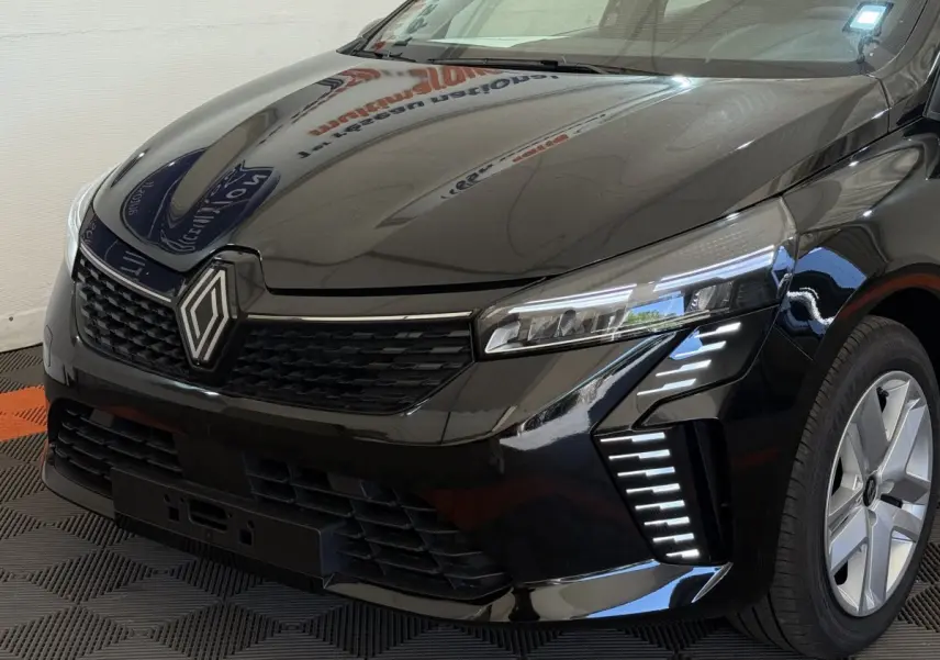 Vue 3/4 avant droit d'une Renault Clio noire 2025 avec phares LED et calandre noire distinctive.