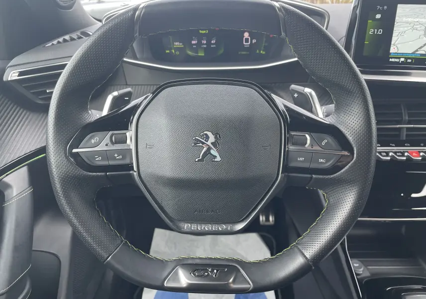 Vue rapprochée du volant cuir perforé noir avec surpiqûres vertes et logo GT du Peugeot 2008 gris Artense 2022.
