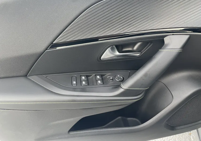Gros plan sur la porte côté gauche du Peugeot 2008 gris Artense, montrant les commandes de vitres et la poignée intérieure.