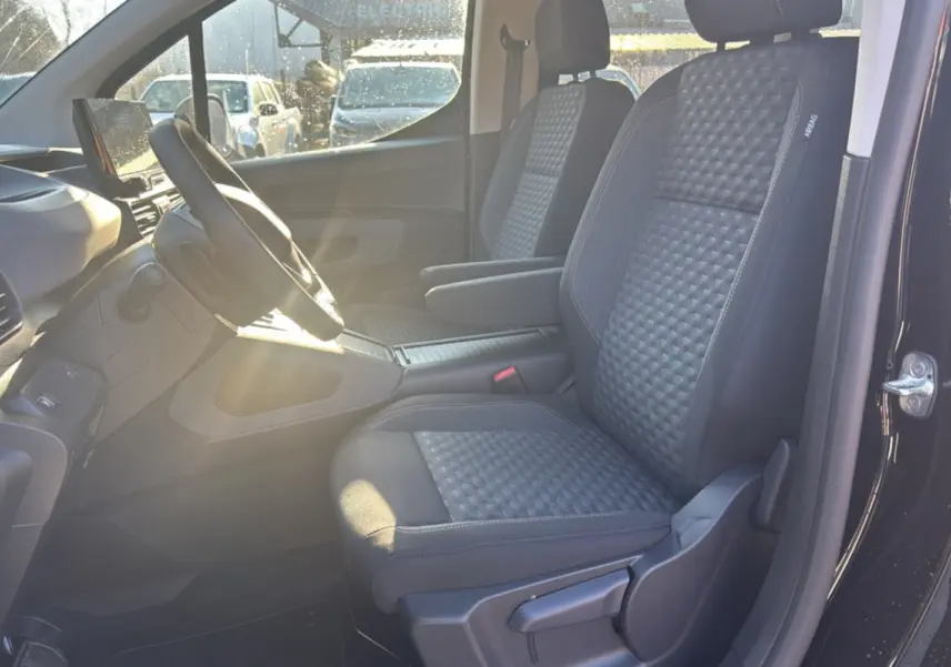 Intérieur avant droit du Peugeot Rifter noir perla nera 2025, sièges tissu gris avec accoudoir central et volant multifonctions.