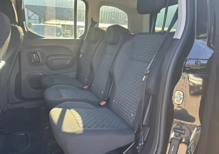Vue latérale intérieure sur les sièges arrière tissu gris du Peugeot Rifter Noir Perla Nera 2025 avec porte ouverte.