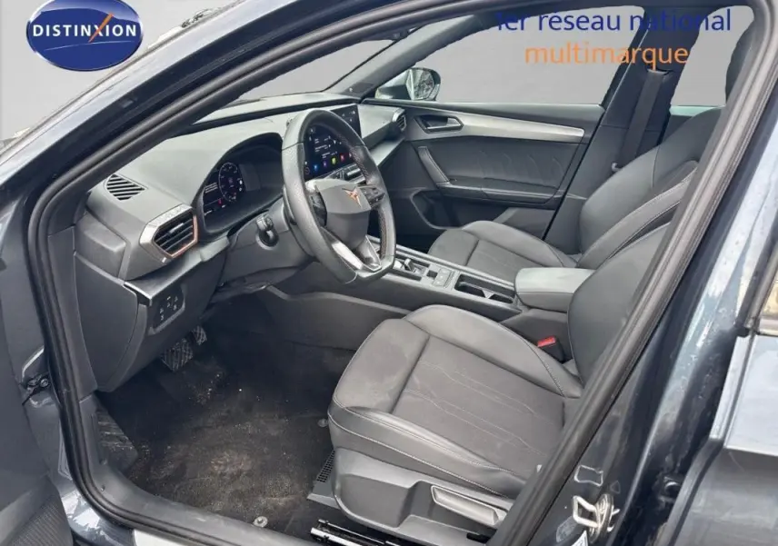 Vue intérieure côté conducteur d'une CUPRA Leon ST gris 2024 avec tableau de bord numérique et volant cuir.