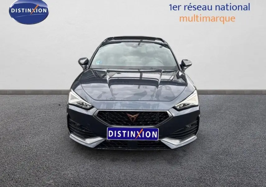 Vue avant d'une CUPRA Leon ST gris foncé avec calandre noire et logo distinctif, stationnée devant un mur clair.