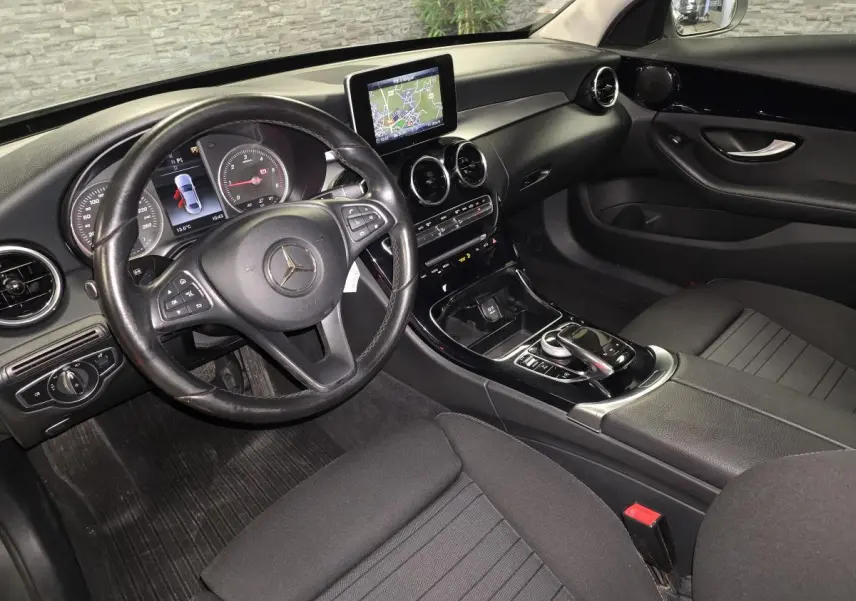 Vue intérieure côté conducteur de la Mercedes Classe C 200 d 2018 avec tableau de bord noir et écran central de navigation.