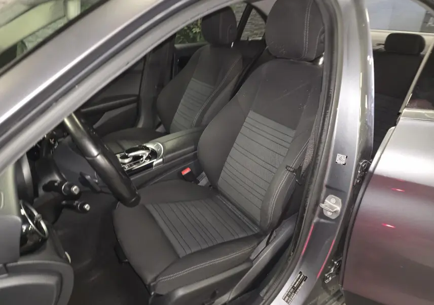 Vue intérieure côté conducteur d'une Mercedes Classe C gris métallisé, sièges avant en tissu noir avec console centrale.