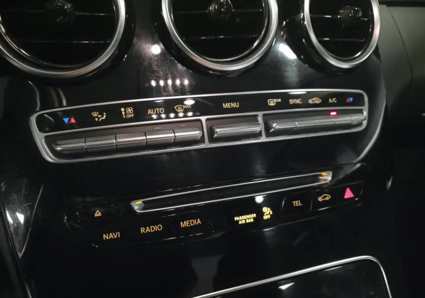 Gros plan sur la console centrale noire brillante de la Mercedes Classe C 200 d, avec commandes climatisation et multimédia.