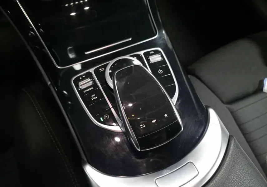 Vue rapprochée de la console centrale noire brillante avec pavé tactile et commandes sur Mercedes Classe C gris.