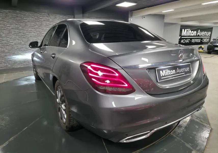 Vue 3/4 arrière gauche d'une Mercedes Classe C gris métallisé avec feux arrière LED allumés en intérieur showroom.