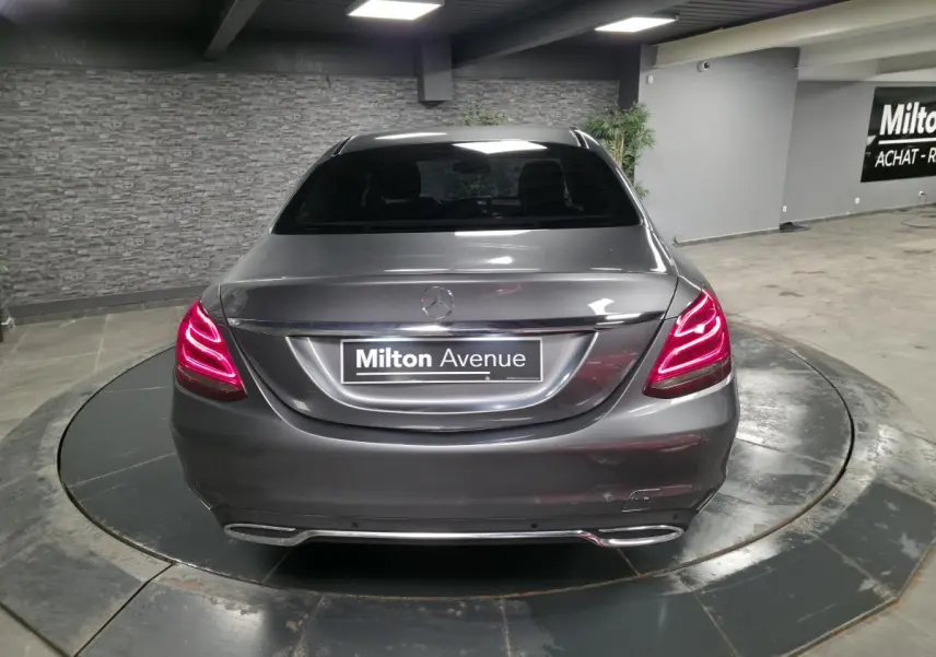 Vue arrière d'une Mercedes Classe C gris métallisé avec feux arrière LED allumés dans un showroom.