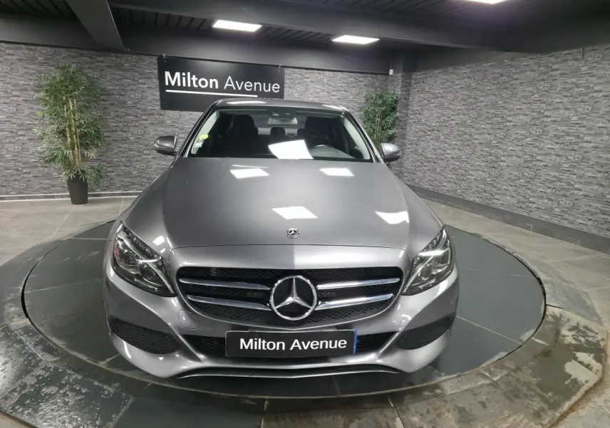 Vue avant d'une Mercedes Classe C gris métallisé avec calandre à deux lamelles et logo étoile central, en showroom.