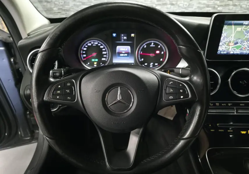 Vue rapprochée du volant noir multifonctions d'une Mercedes Classe C 2018 avec tableau de bord et écran de navigation visibles.