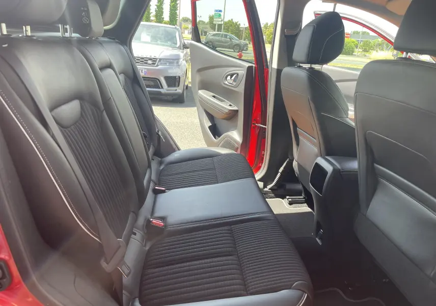 Vue intérieure arrière côté gauche du Renault Kadjar rouge flamme, montrant les sièges noirs en cuir et tissu avec porte ouverte.