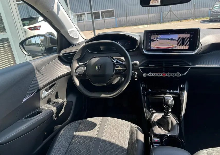 Vue intérieure avant de la Peugeot 208 1.2 100ch gris Selenium, volant compact et écran tactile avec caméra de recul visible.