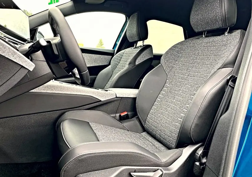 Vue intérieure côté conducteur du Peugeot 3008 bleu 2025, mettant en valeur les sièges bi-matière gris et noir et le volant cuir.