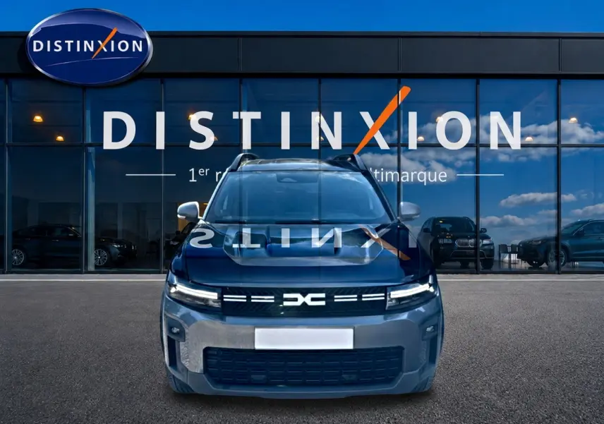 Vue avant d’un Dacia Bigster gris schiste stationné devant une vitrine avec logo Distinxion en reflet sur le capot.