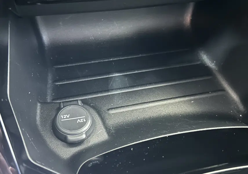 Gros plan sur la prise 12V dans la console centrale d’un Peugeot 2008 noir hybride, intérieur sobre et fonctionnel.
