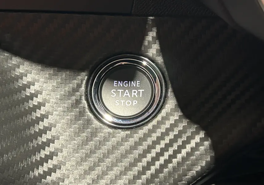 Bouton start/stop moteur en gros plan sur console avec finition carbone du Peugeot 2008 II Hybrid 110 Allure noir.
