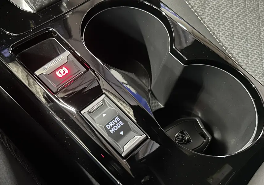 Gros plan sur la console centrale noire du Peugeot 2008 II Hybrid avec bouton Drive Mode et frein à main électronique allumé.