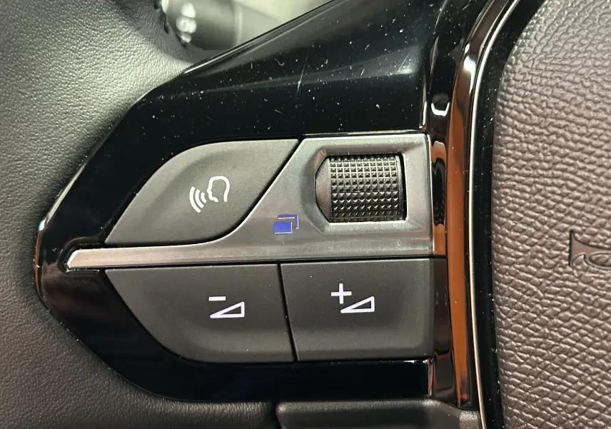 Gros plan sur les commandes de volume et téléphone sur le volant noir du Peugeot 2008 II Hybrid 110 Allure.