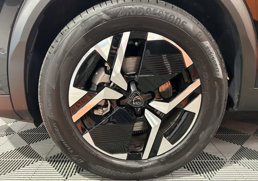 Gros plan sur la roue avant gauche du Peugeot 2008 noir, mettant en valeur la jante alliage bicolore et le pneu Bridgestone.