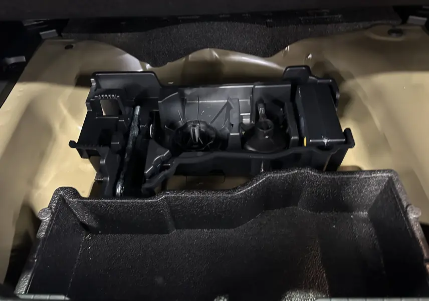 Coffre ouvert d’un Peugeot 2008 noir, vue plongeante sur le rangement interne et compartiment à outils.