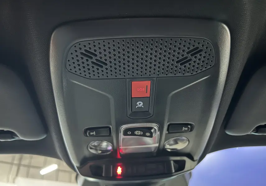 Vue en contre-plongée du panneau de commandes de toit intérieur noir du Peugeot 2008 II Hybrid, avec bouton SOS rouge et éclairages.