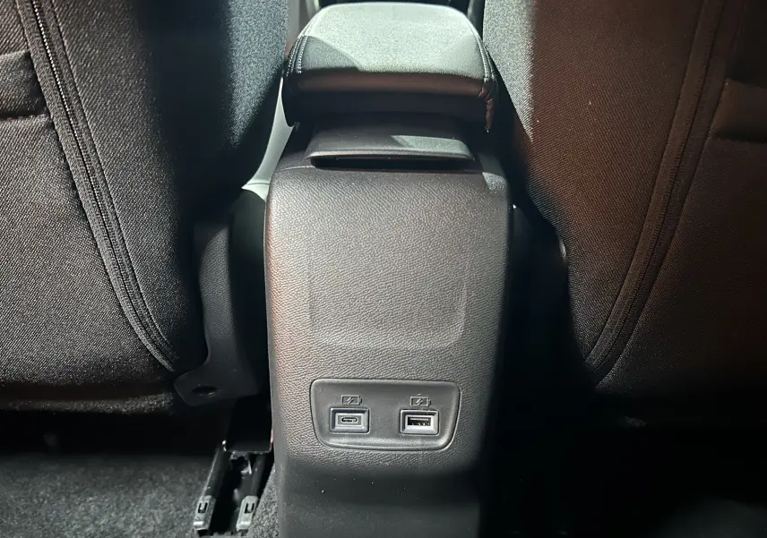 Vue rapprochée de la console centrale arrière noire du Peugeot 2008 II Hybrid avec ports USB-C et USB-A visibles.