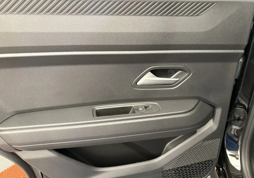 Vue rapprochée de la porte intérieure côté conducteur du Dacia Duster noir, avec poignée et commande de fenêtre.