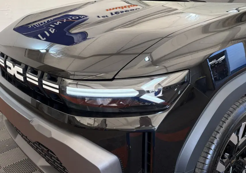 Gros plan sur l'avant droit du Dacia Duster noir 2025, mettant en valeur le phare LED et la calandre distinctive.