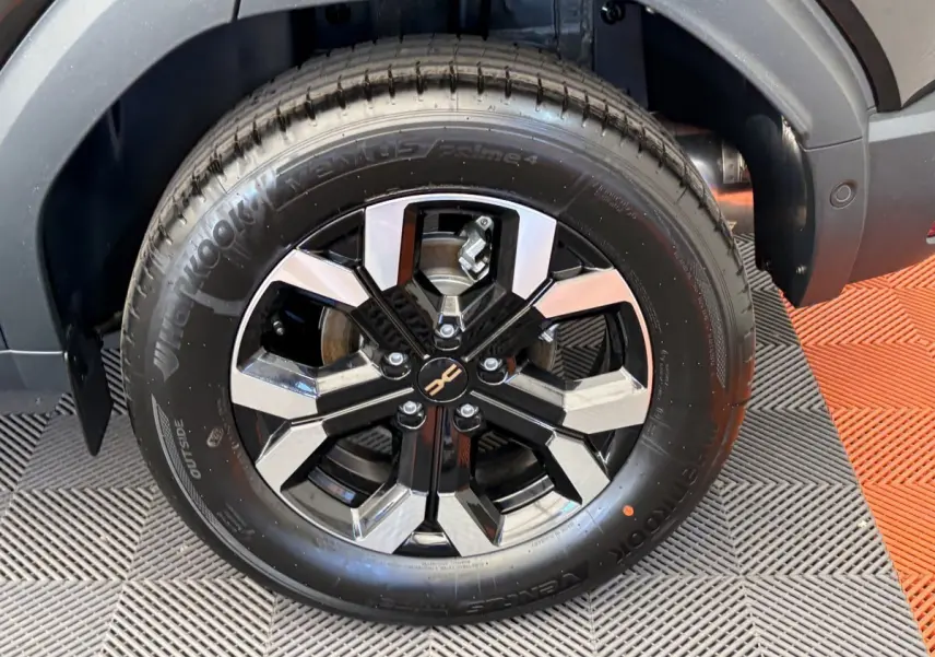 Gros plan sur la roue avant droite du Dacia Duster noir 2025 avec jante alliage bicolore et logo central distinctif.